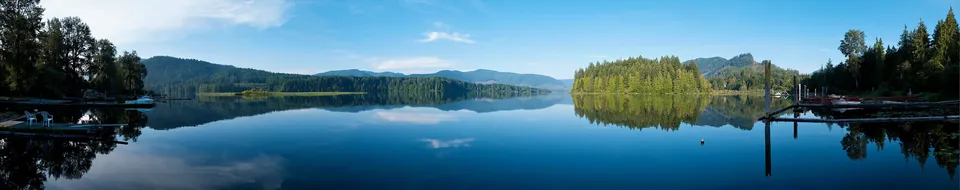 Panorama of a still bay at Cowichan Lake at dawn with docks and forested shore
