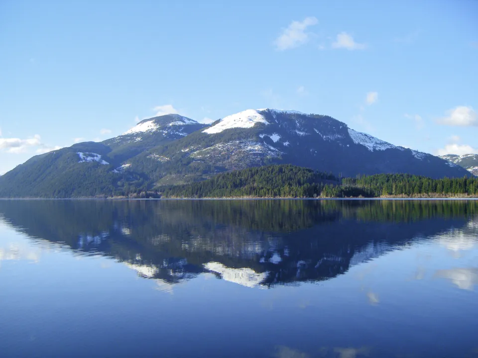 Snow-capped forested mountains reflected in a calm Cowichan Lake